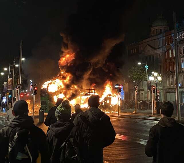 Passers by watching a bus burning in Dublin, set alight by far right protestors.